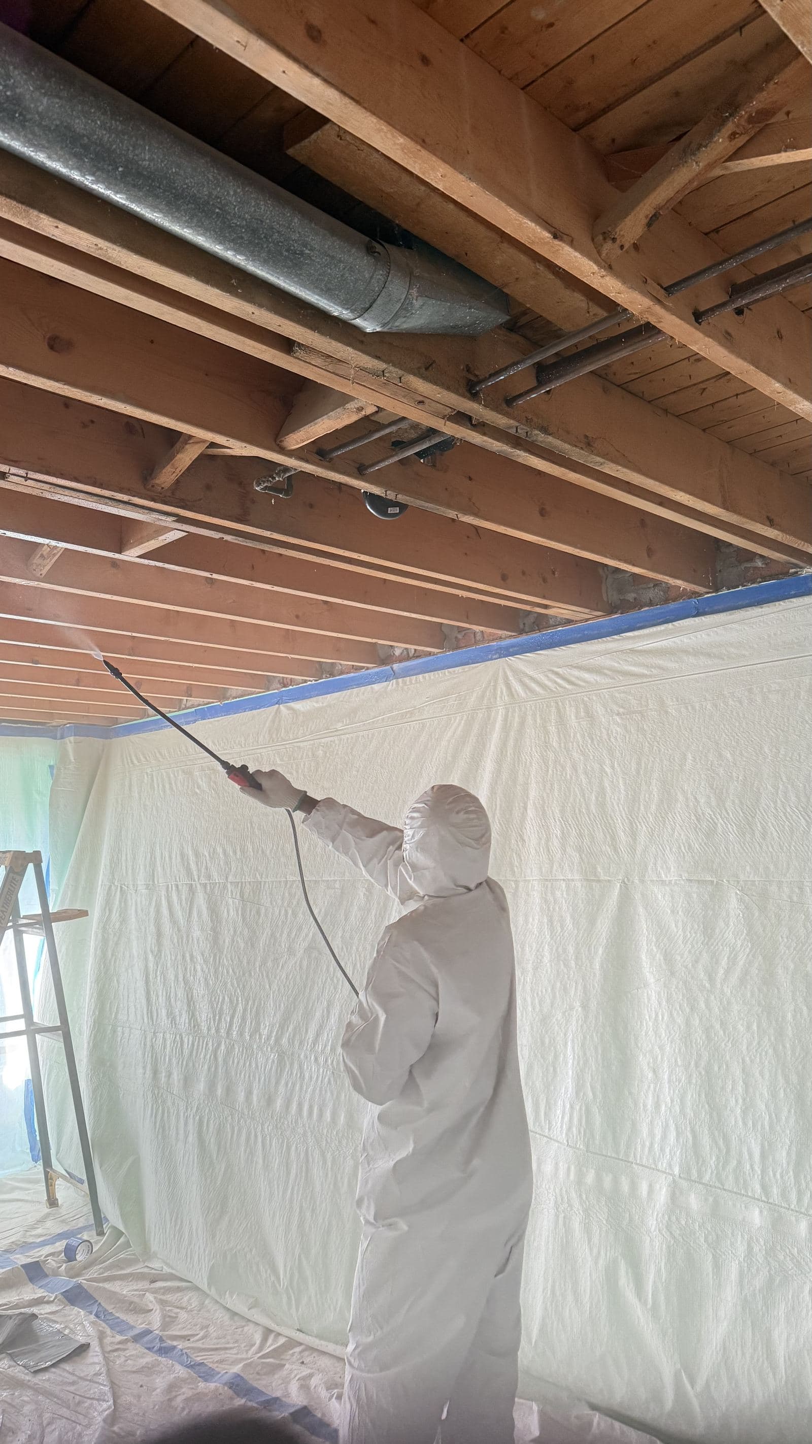 Worker treating sealed containment sheeting below exposed joists